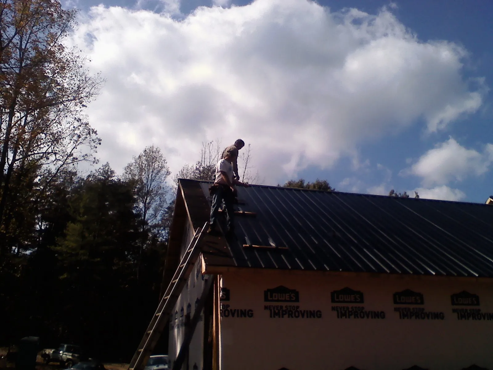 Roofer fastening dark metal panels high against a cloudy sky, from a Roof Inspection job in Saratoga